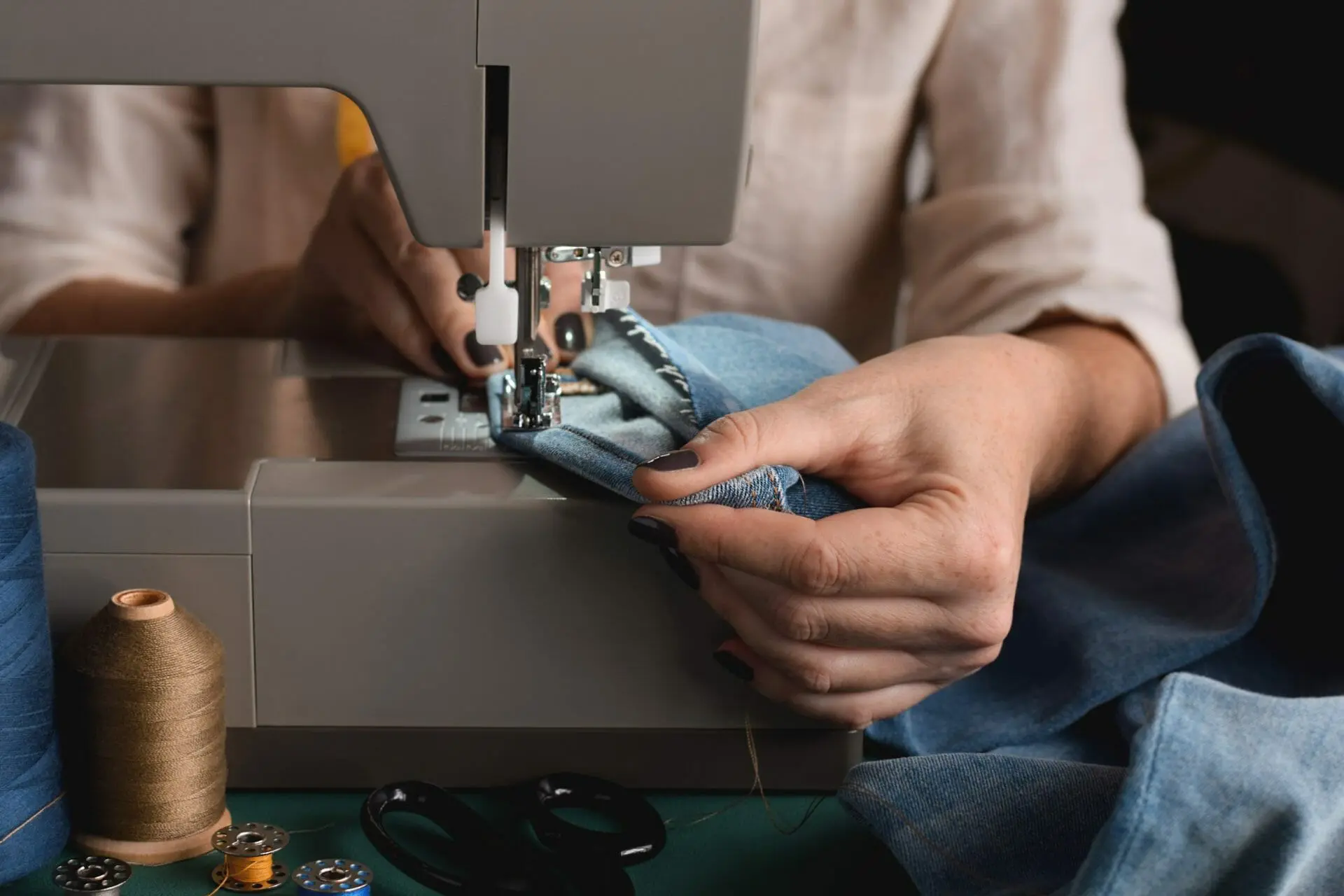 A woman is sewing a pair of jeans on a sewing machine.