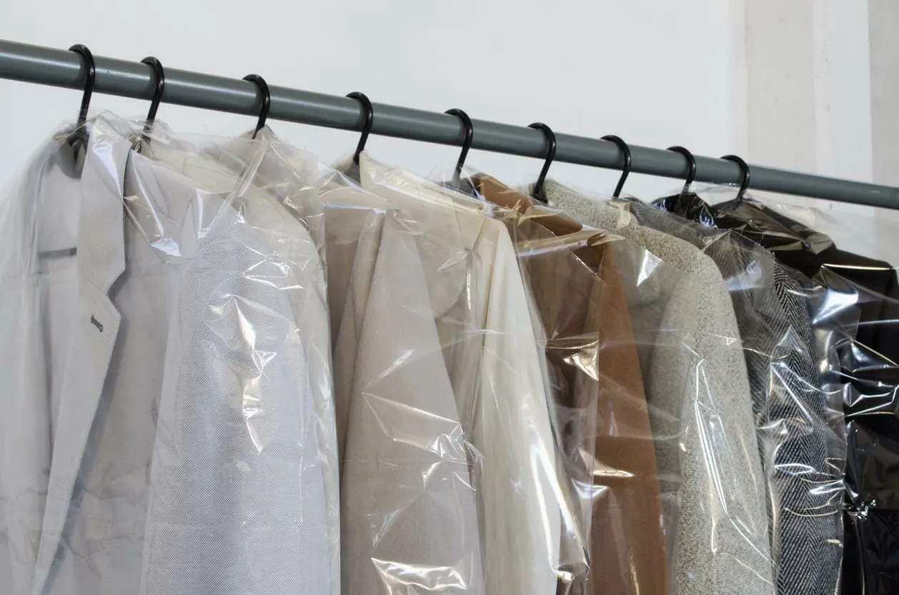 A rack of clothes in plastic bags hanging on a rack.
