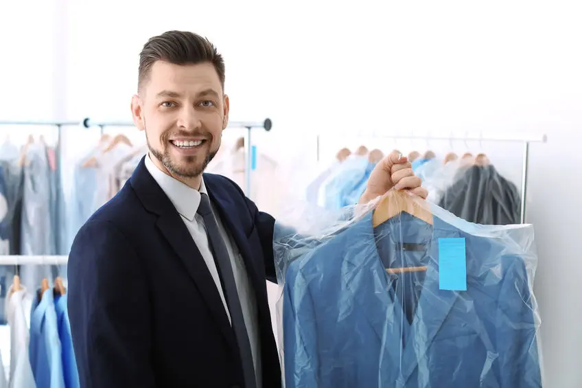 A man in a suit holding a plastic hanger in a laundry room.