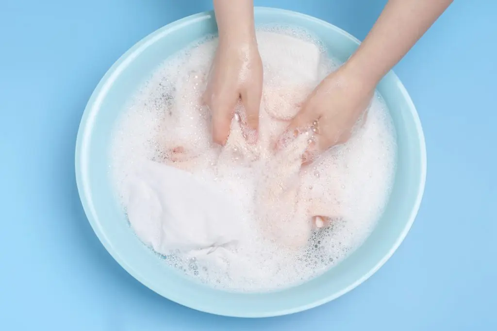 Hands washing clothes in a blue basin filled with soapy water.