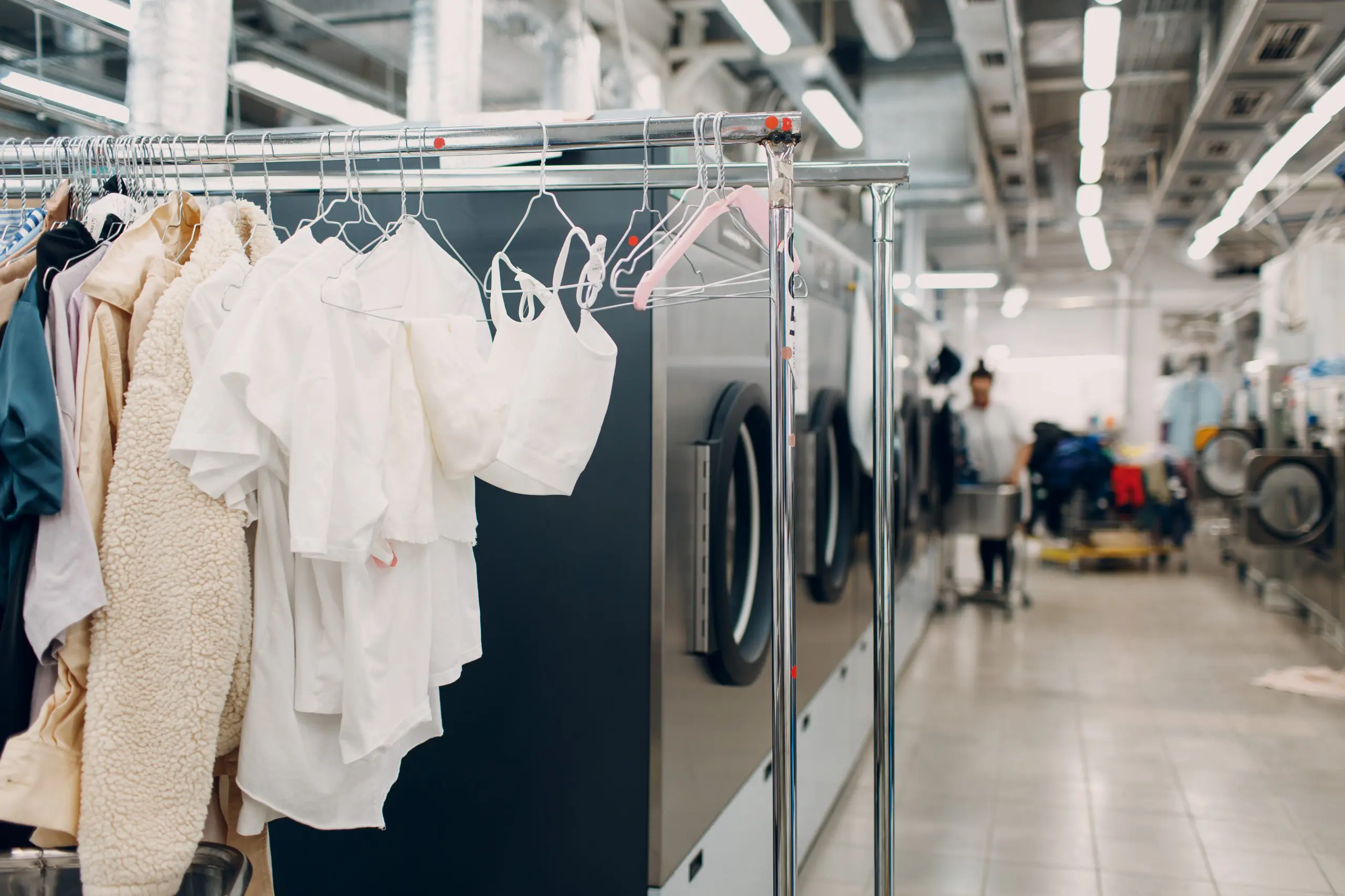 Clothes hanging on a rack in a busy laundromat with washing machines in the background.