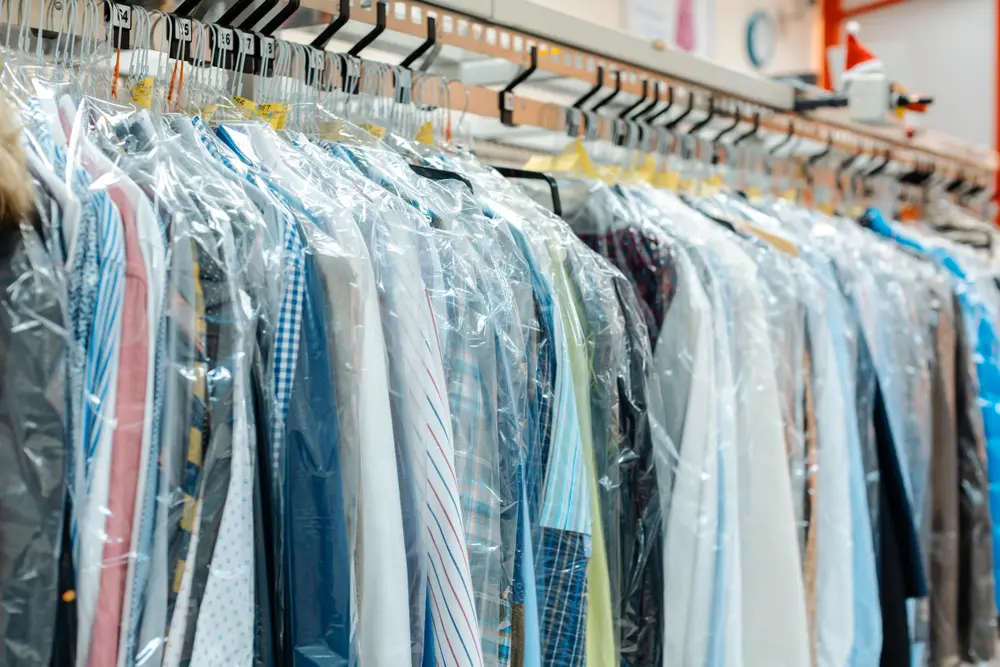 A row of clothes covered in plastic hanging on a conveyor system in a dry cleaning shop in Marshall, TX showcases their commitment to quality service.